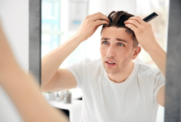 Mann schaut fragend in den Spiegel und untersucht seine Haare