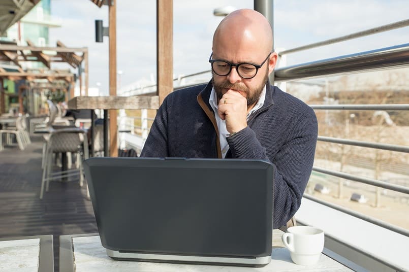 Mann mit Glatze sitzt nachdenklich in einem Cafe mit offenem Laptop