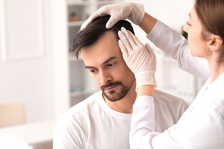Bild zeigt, wie eine Ärztin bei einem Patienten den Haarausfall prüft