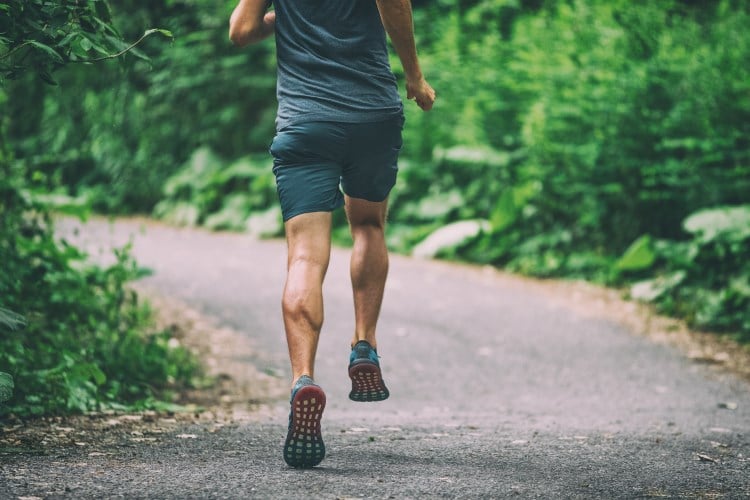 Die Beine eines Mannes von hinten, der auf einem Weg joggt