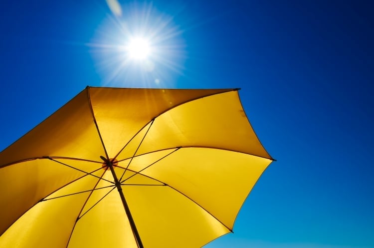 Die Sonne am blauen Himmel scheint auf einen gelben Sonnenschirm