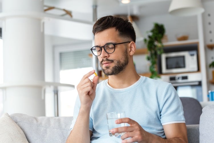 Mann nimmt eine Tablette und hält ein Glas Wasser in der Hand