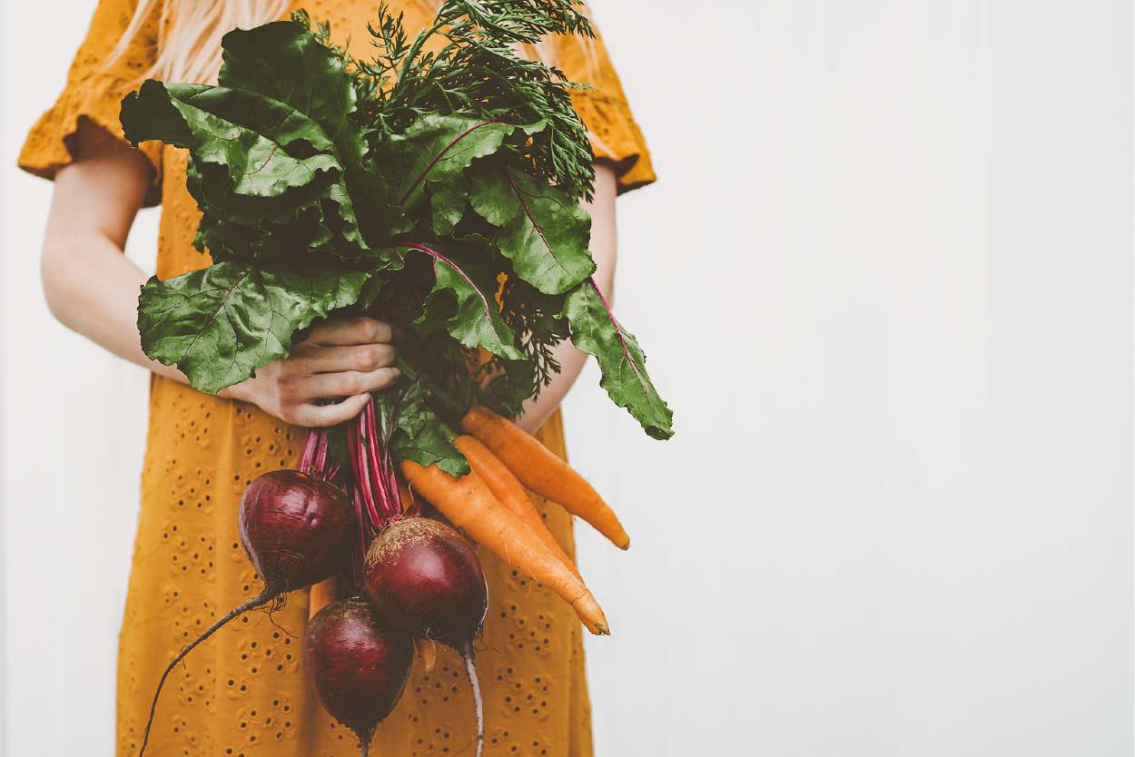 Mujer sosteniendo zanahorias y remolachas