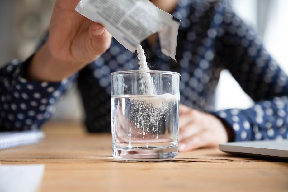 Mujer echando un medicamento en polvo en un vaso de agua. Ciertos fármacos pueden ser una de las causas de la caída del cabello en mujeres