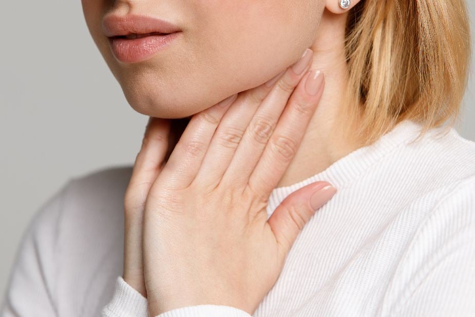 Mujer tocándose la glándula tiroides bajo el cuello