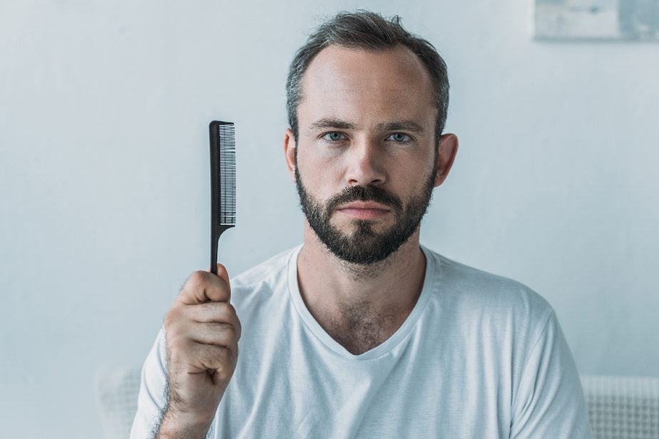 Hombre con un peine en la mano mostrando los efectos de la caída de pelo
