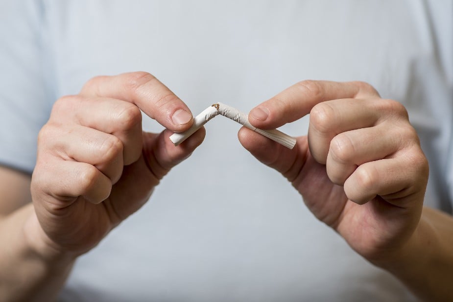 Hombre rompiendo un cigarrillo por la mitad.