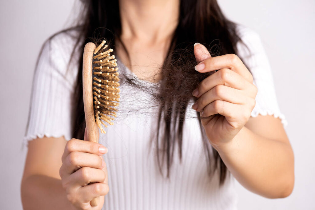 A woman pulls a large clump of hair from a hairbrush.
