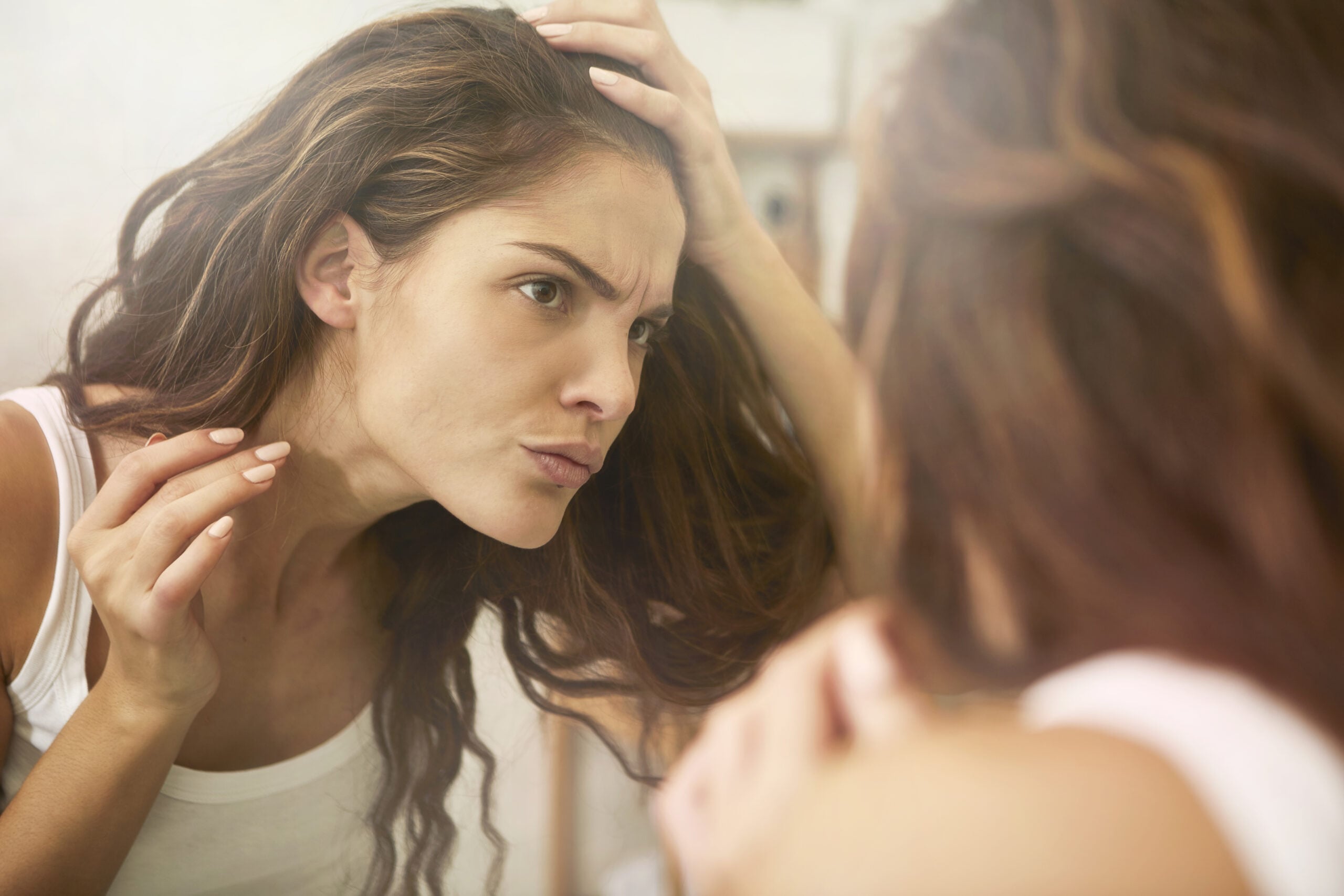Woman looking in mirror for hair shedding.