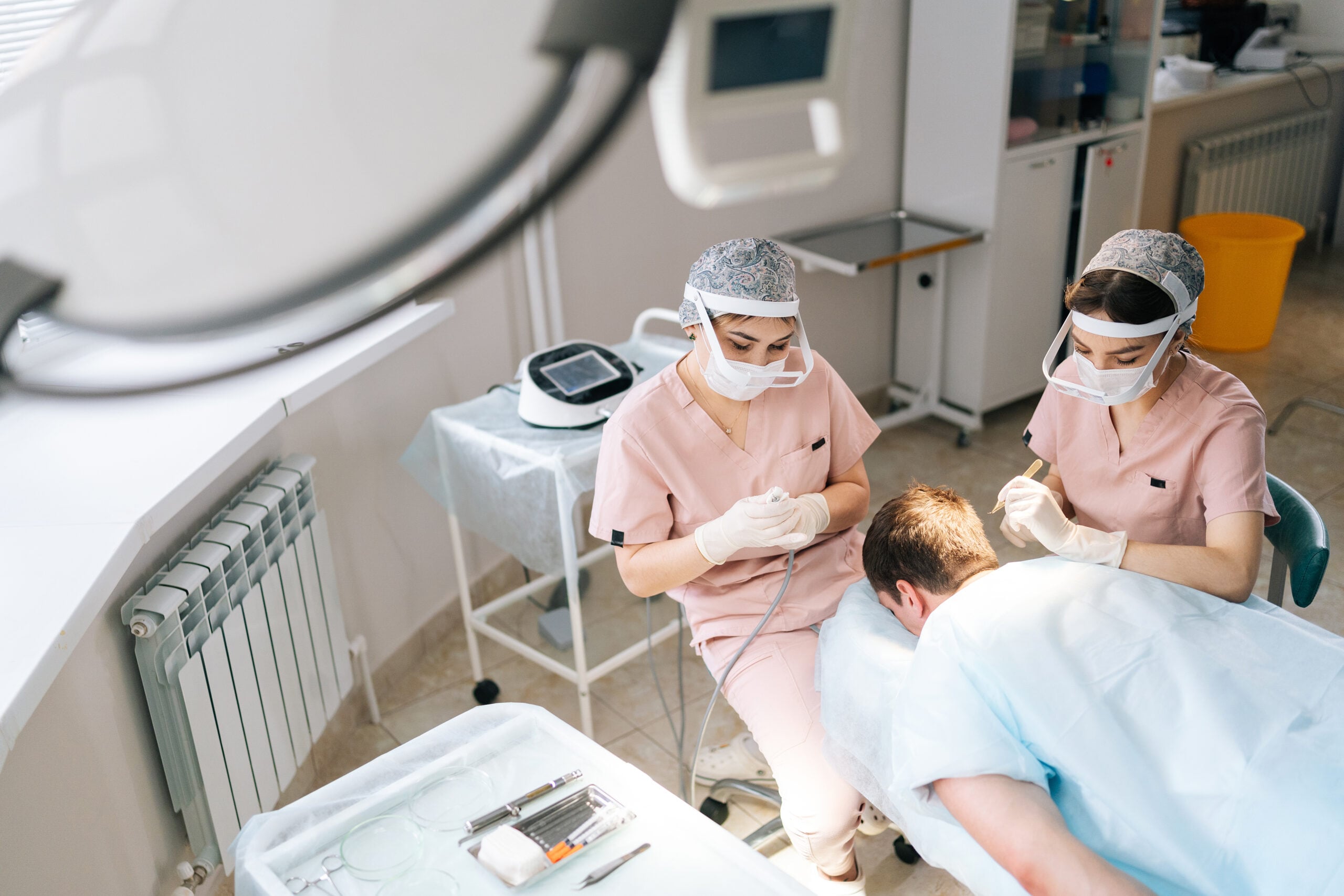 Two female medical technicians perform a follicular unit extraction on a male patient.