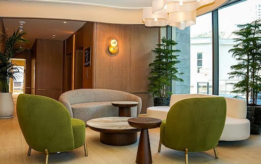 A modern lounge in the Elitoria Hotel featuring stylish green and neutral-coloured furniture, with lots of natural light.