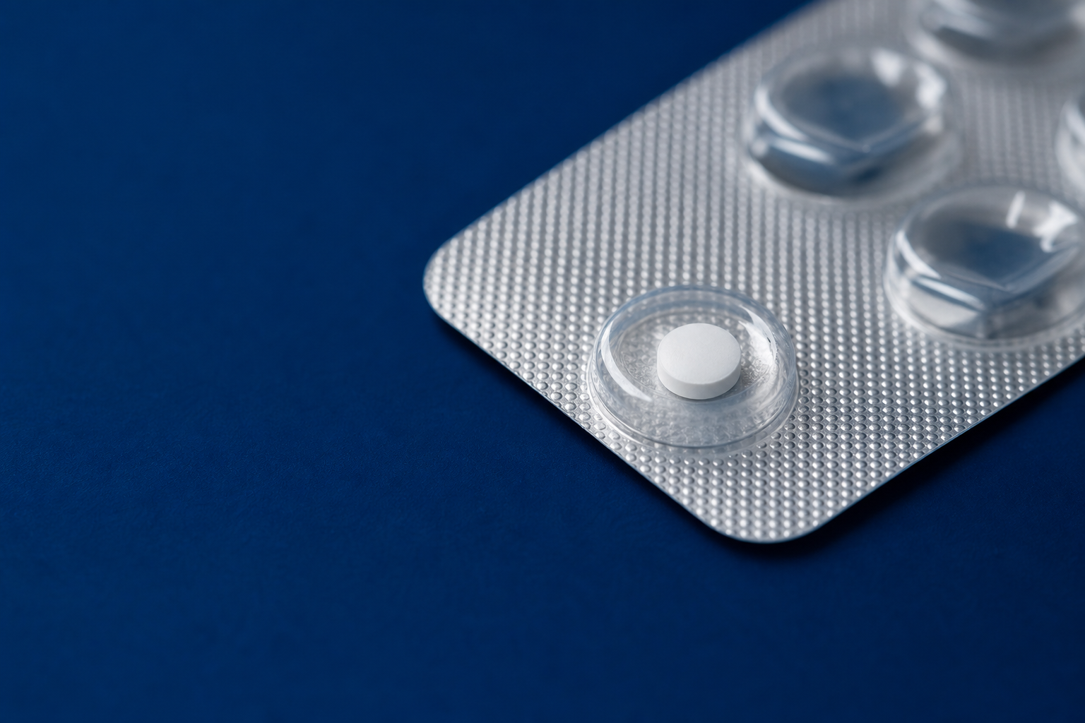 Einzelne Finasterid-1-mg-Tablette in einem Blister auf dunkelblauem Untergrund
