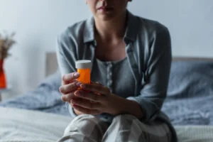 A menopausal woman holding a prescription pill bottle while sitting on her bed.