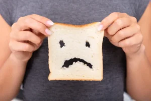 A person holding up a slice of white bread that has a frowny face cut into it.