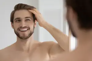 A man stands before a mirror and happily runs his fingers through his hair.