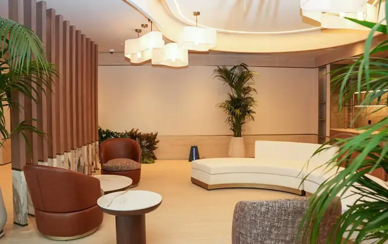 A modern lounge area at the Elitoria Hotel with a curved sofa, leather armchairs, and potted palm trees