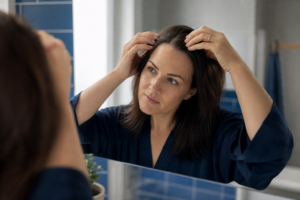 Person calmly examining their hair at the part in the mirror, getting to the bottom of the causes of hair loss