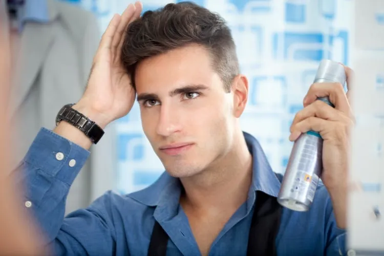 Man setting his styled hair with hairspray while running a hand through it