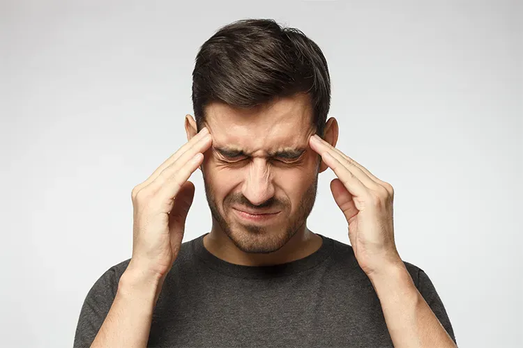 A man holds his head with both hands, eyes squeezed shut, conveying a feeling of tightness and a scalp that is painful to touch
